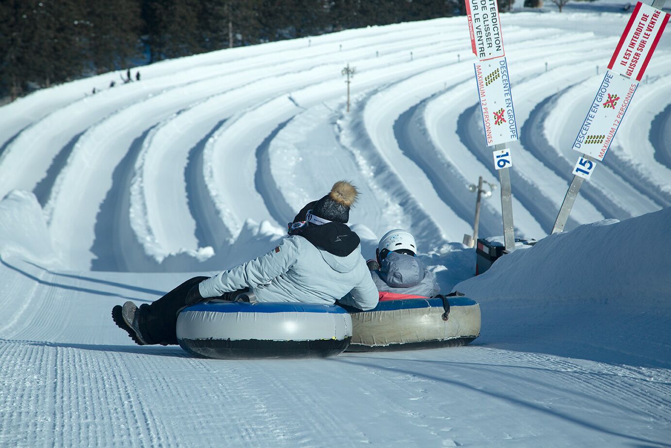 Dos personas bajando por una pendiente nevada en un trineo inflable azul.