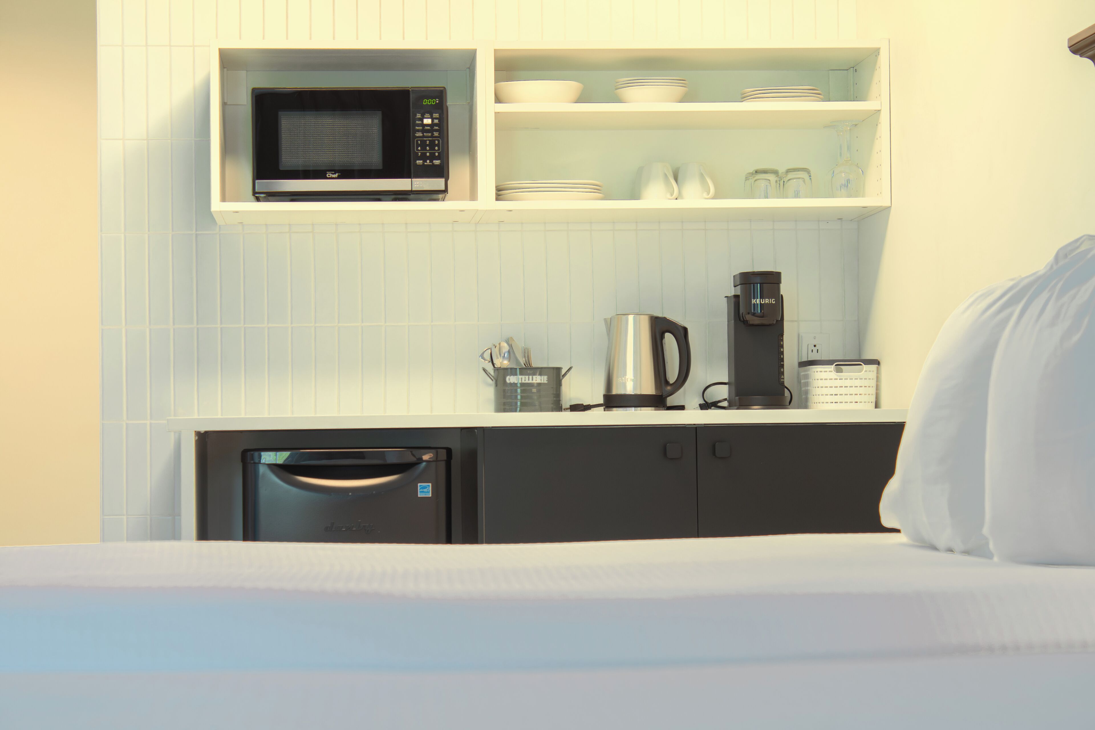A compact kitchenette with a microwave, coffee maker, and storage cabinets.