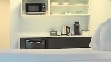 A compact kitchenette with a microwave, coffee maker, and storage cabinets.