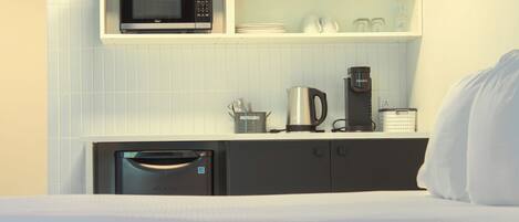 A compact kitchenette with a microwave, coffee maker, and storage cabinets.
