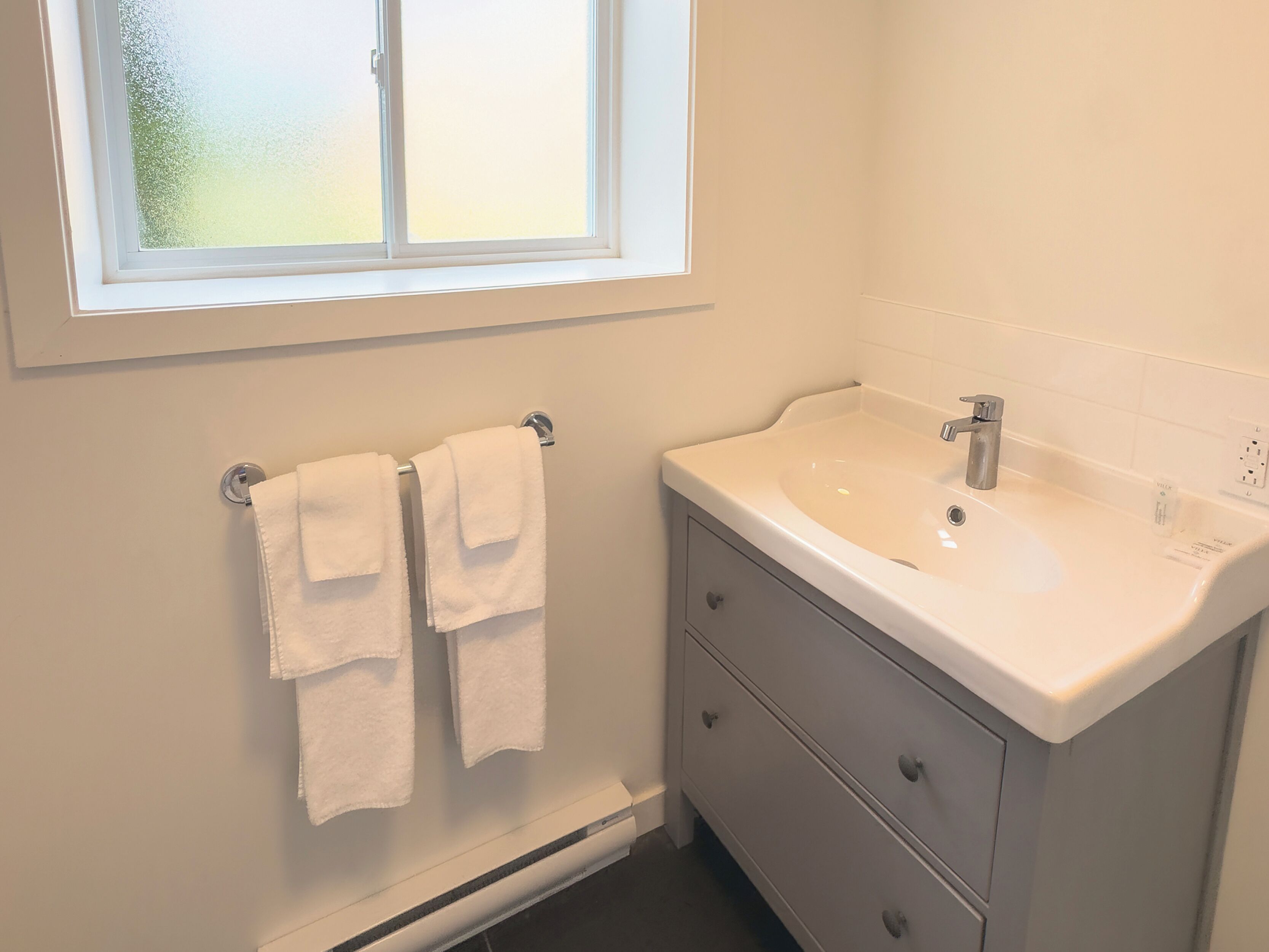 A bathroom with a window, a sink, and two towels hanging on a rack.