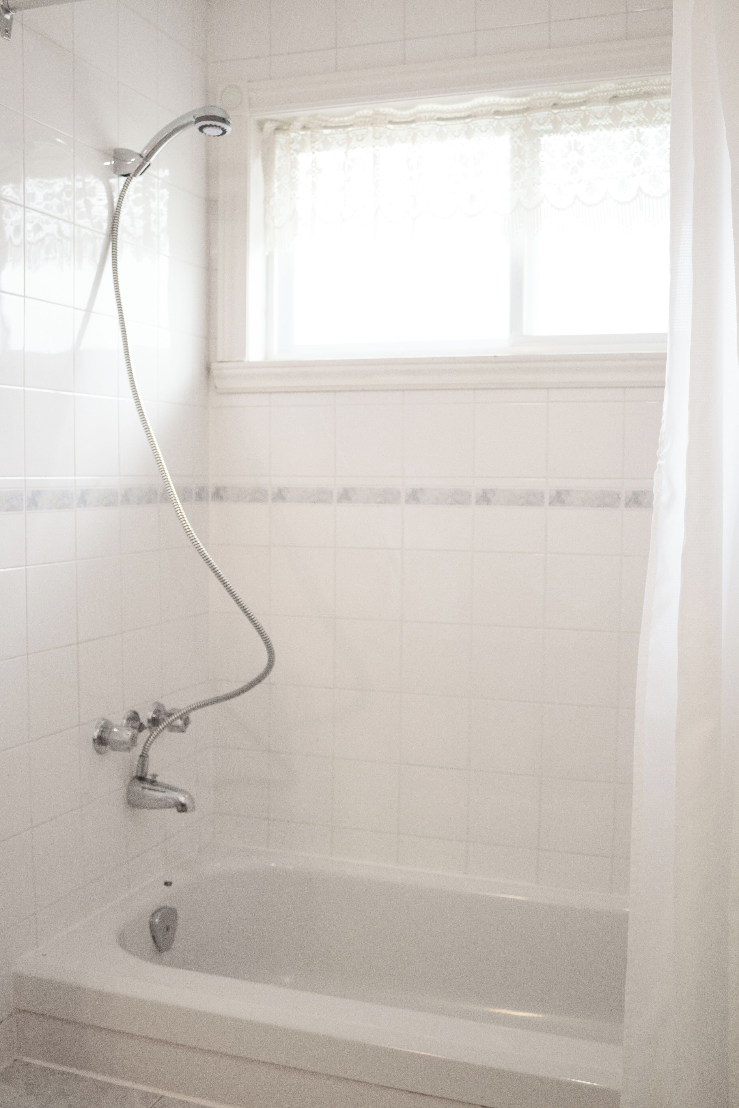 A bathroom with a bathtub, a shower, and a window with a curtain.