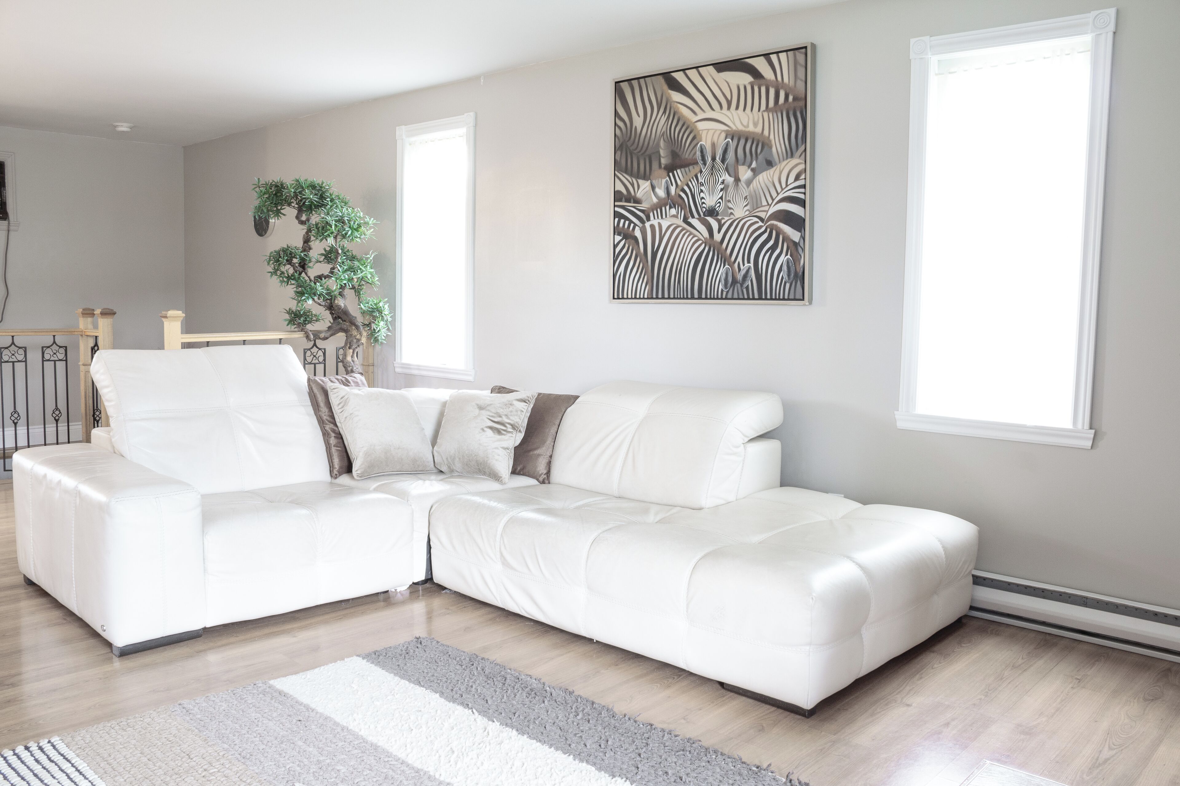 A modern living room with a white sectional sofa, a large abstract painting, and a potted plant.