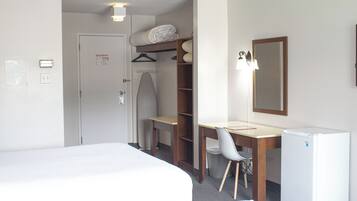 A hotel room with a bed, a desk, a chair, a wardrobe, and a small refrigerator.