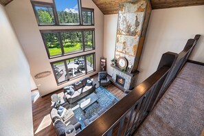 A spacious living room with a fireplace, large windows, and a view of the outdoors. - Sunrise Pines In Powder House Pass (South Lawrence)