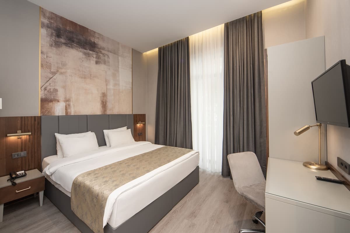 A modern hotel room with a large bed, bedside tables, a desk, and a television.