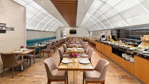 Un grand espace dédié à la salle à manger, avec de longues tables, des sièges confortables et un comptoir de cuisine où sont exposés des plats.