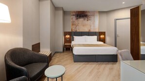 Une chambre d’hôtel moderne, dotée d’un grand lit, d’une chaise, d’une petite table et d’un luminaire fixé au mur.