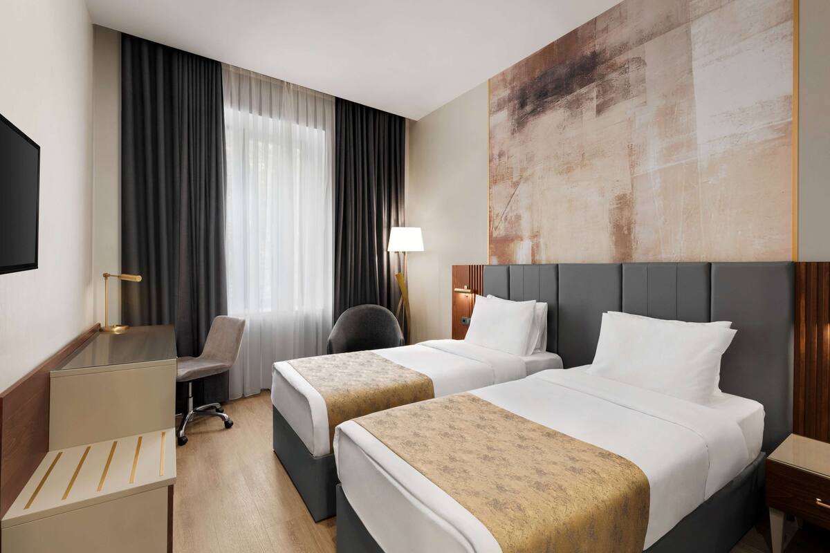 A hotel room with two beds, a desk, a chair, and a large abstract painting on the wall.