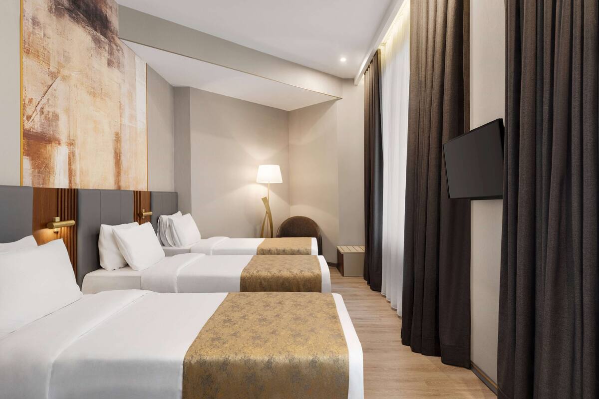A hotel room with two beds, a large abstract painting on the wall, a lamp, and dark curtains.