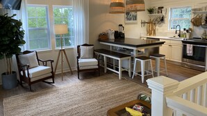 A modern kitchen with a central island, pendant lights, and a dining area with chairs.