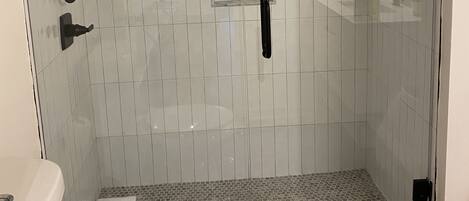 Ducha envuelta en vidrio con cabezal de ducha manual y llave en la pared.