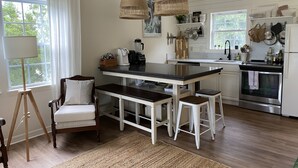 A modern kitchen with a central island, white cabinetry, and a dining area with a chair and bench.