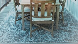 Una terraza de madera con una mesa, sillas y una sombrilla, con vistas al exterior.