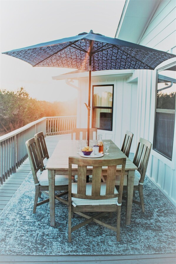 A wooden deck with a table and chairs, an umbrella, and a view of the outdoors.