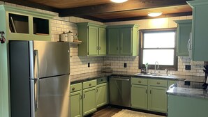 Una cocina con armarios verdes, un refrigerador de acero inoxidable y techo de madera.