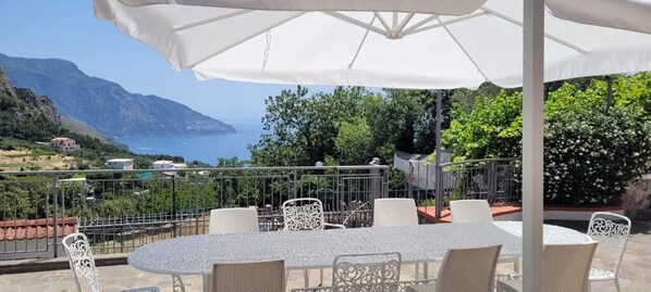 An outdoor patio with a round table and chairs, overlooking a scenic view of the sea and mountains. - Villa Cristina (Piano di Sorrento)
