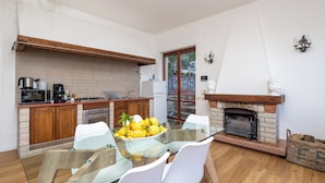 A modern kitchen with a glass dining table, white chairs, and a stone fireplace. - Villa Cristina (Piano di Sorrento)