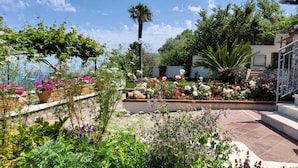 A garden with various plants and flowers, a palm tree, and a staircase leading to a building. - Villa Cristina (Piano di Sorrento)