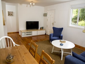 A living room with a TV, a blue armchair, a round white table, and a wooden dining table.
