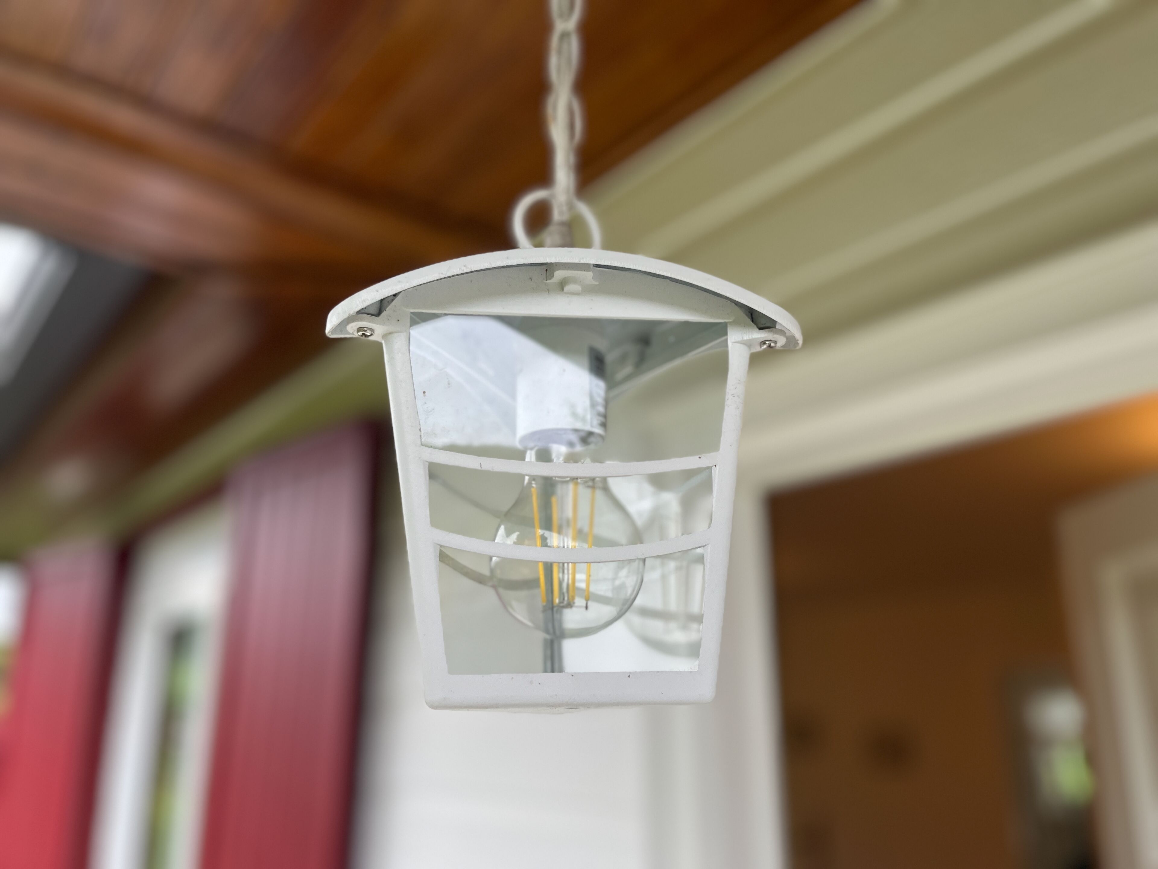 A hanging lantern with a clear glass enclosure and a visible light bulb filament.
