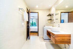 A modern bathroom with a large mirror, a wooden vanity, and a view of a balcony. - The Title Condo Phase 3 by Lofty (Rawai)