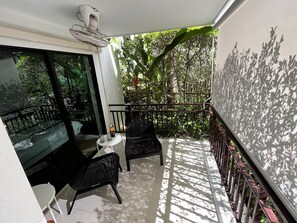 A balcony with a glass table, two chairs, a ceiling fan, and a view of dense greenery. - The Title Condo Phase 3 by Lofty (Rawai)