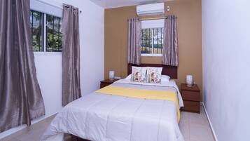 A bedroom with a bed, nightstands, an air conditioner, and curtains.