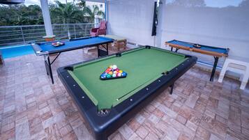 Une table de billard recouverte d’un drap vert, un queue de billard et un jeu de billes.