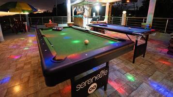 Uma mesa de bilhar com um letreiro neon, cercada por um deck de madeira e área de estar externa.