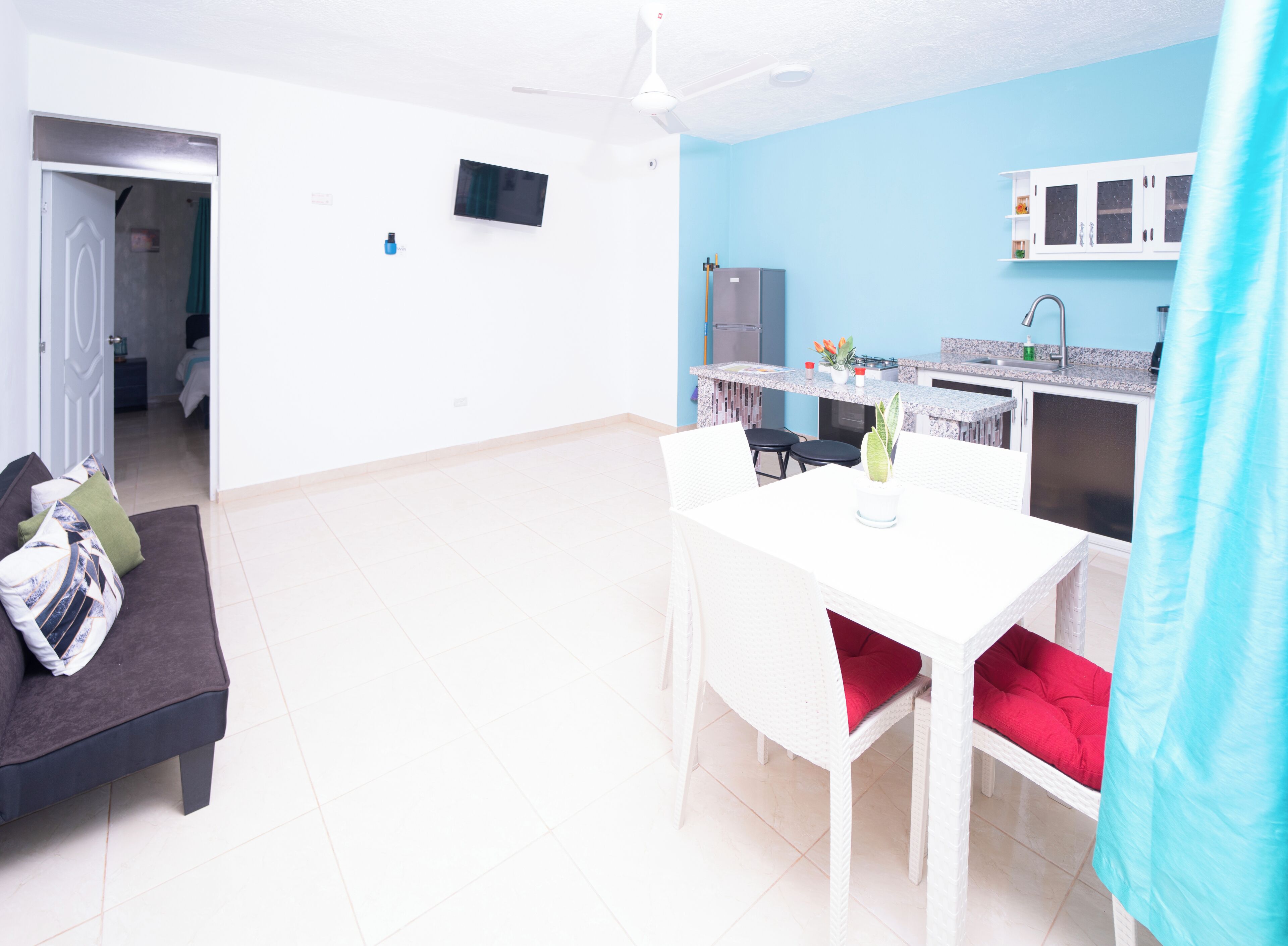 A compact living space with a kitchenette, a dining area with a white table and chairs, and a sofa with cushions.