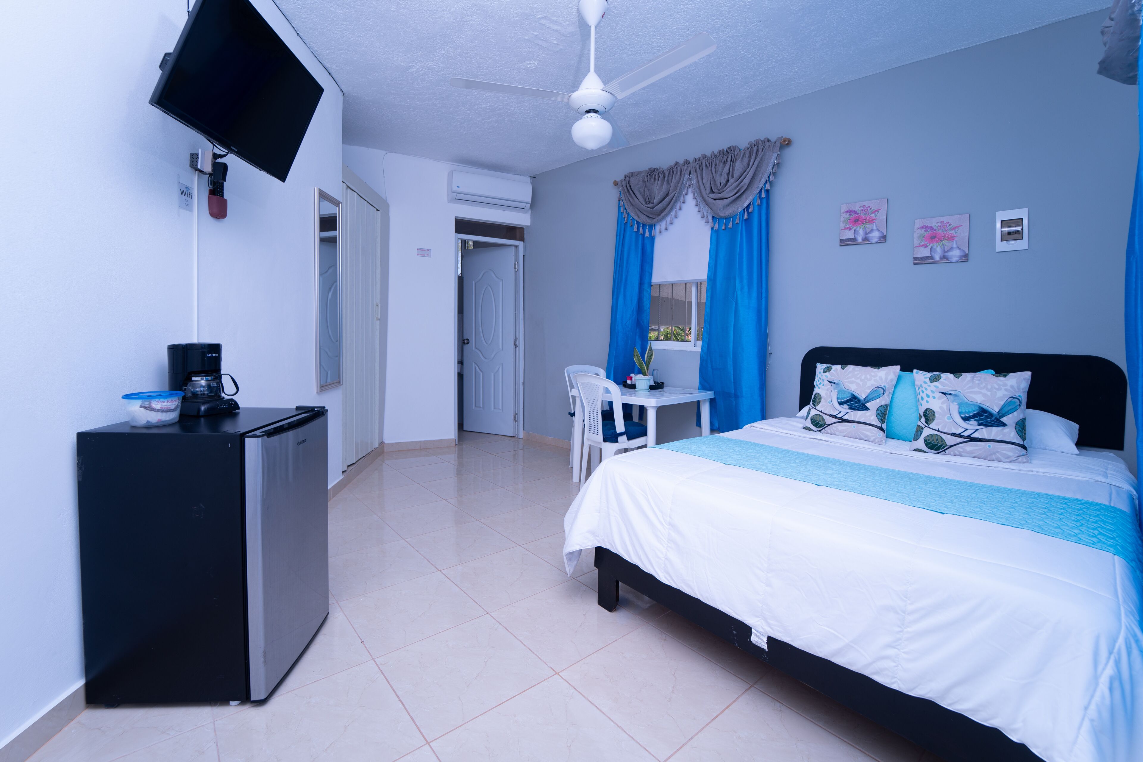 Un dormitorio con cama, escritorio, silla, televisor y refrigerador.
