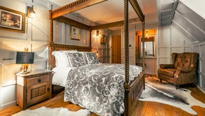 Una cama con dosel con una colcha estampada, una mesita de noche de madera con una lámpara, una silla y una alfombra de piel sobre un piso de madera.