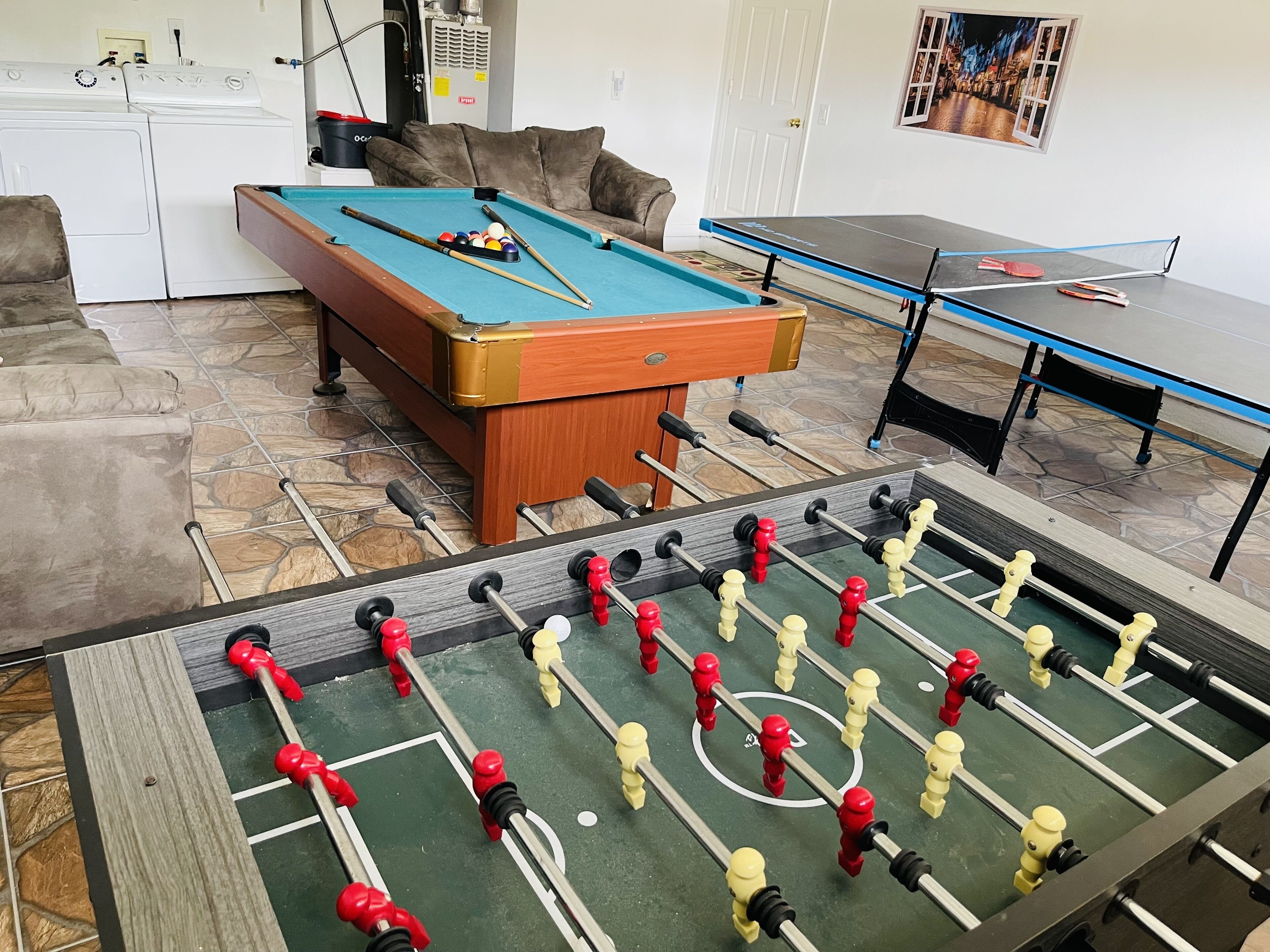 A room with a foosball table, a pool table, and a sofa.