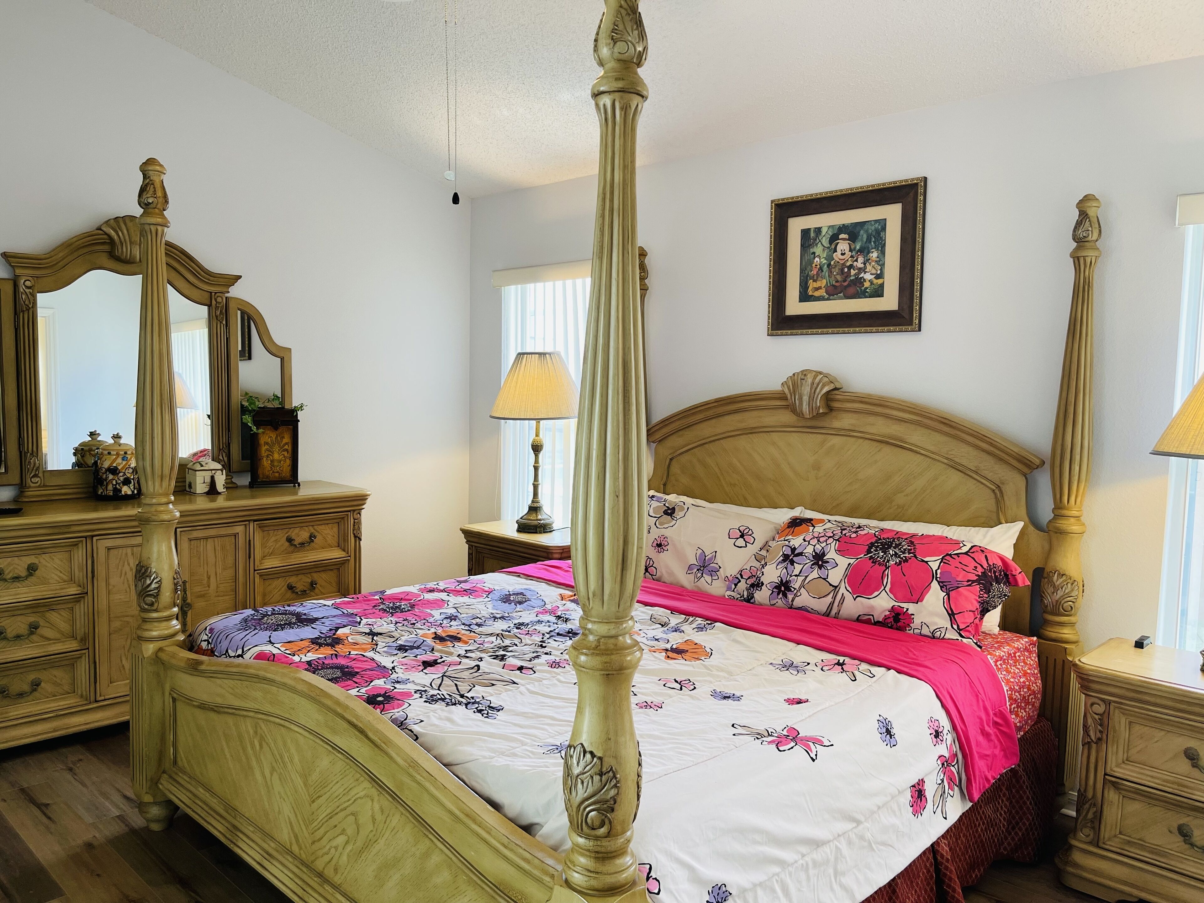 Uma cama com dossel, roupa de cama floral, um espelho e um quadro na parede.