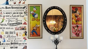 Eine Wand mit Disney-Dekoration, darunter gerahmte Bilder und ein großes Poster mit Text und Figuren.