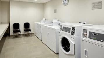 A laundry room with four washing machines, two chairs, and a clock on the wall.