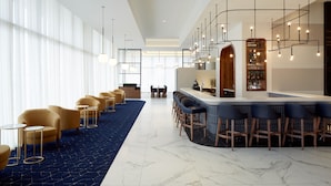 Una hall moderna di un hotel con area bar, posti a sedere e un'ampia finestra che lascia entrare la luce naturale.