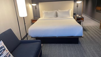 Quarto de hotel com uma cama grande, duas mesas de cabeceira, um criado-mudo, um sofá e um abajur.