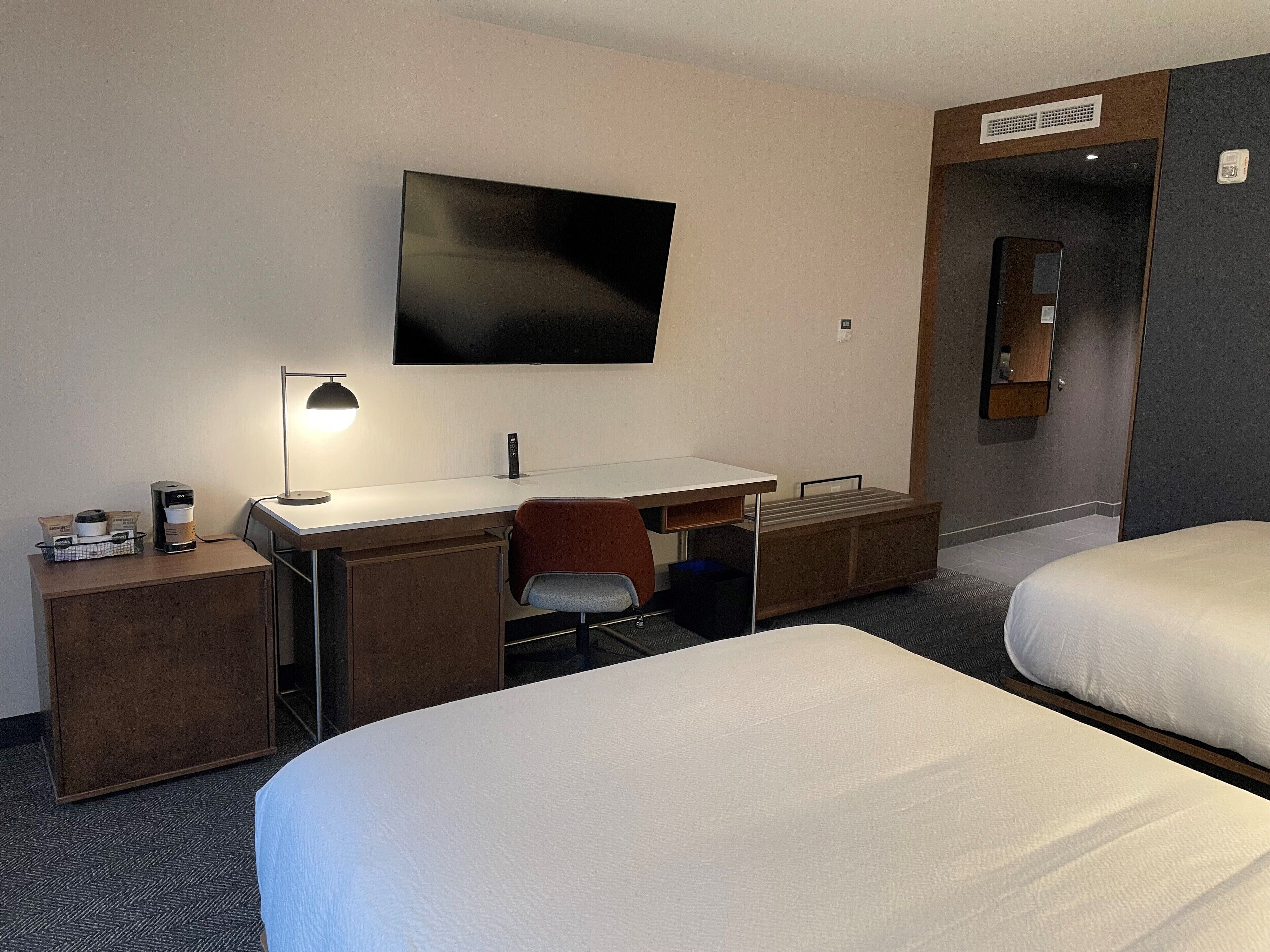 Quarto de hotel com cama, escrivaninha com cadeira, televisão e máquina de café.