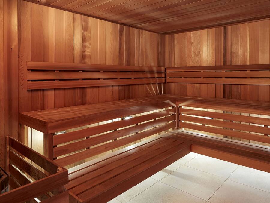 A sauna with wooden benches and walls, tiled floor, and a bench with a backrest.