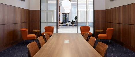 Une salle de conférence avec une longue table, six chaises orange et un lustre moderne.