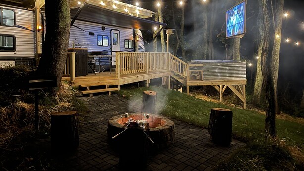 A campsite with a covered dining area, a fire pit, and a TV screen mounted on a tree. - Posh Mountain Camping w/ 120" Screen Theater ·Hot-Tub · Firepit · Hiking Trails (Jonesville)