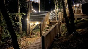 A wooden deck with a staircase leading to a platform, surrounded by trees and string lights. - Posh Mountain Camping w/ 120" Screen Theater ·Hot-Tub · Firepit · Hiking Trails (Jonesville)