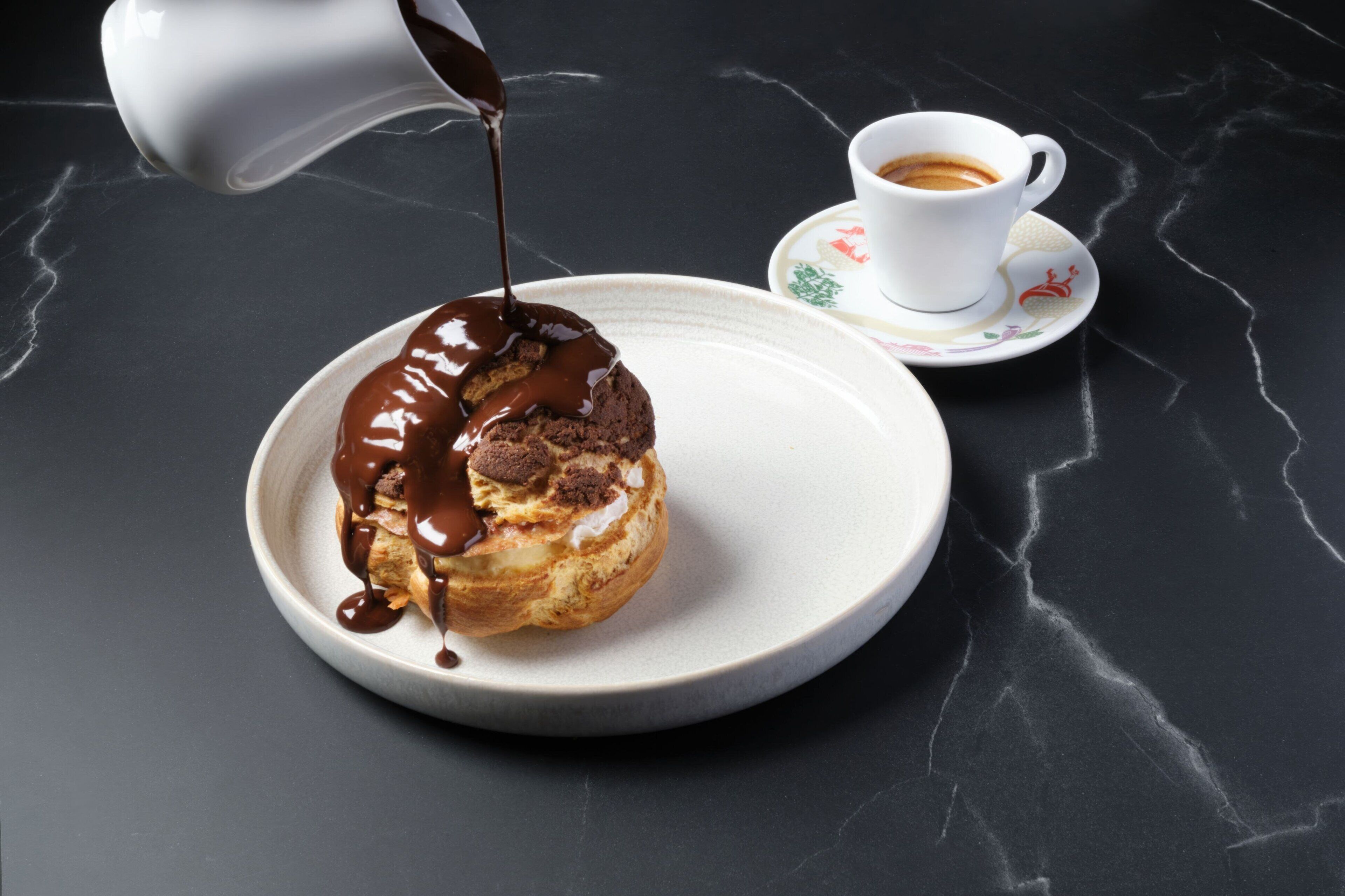 A dessert on a plate with a cup of coffee on a marble table.