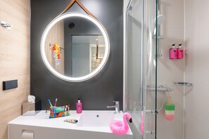 Un baño con espejo redondo, lavabo blanco y cabina de ducha de cristal.