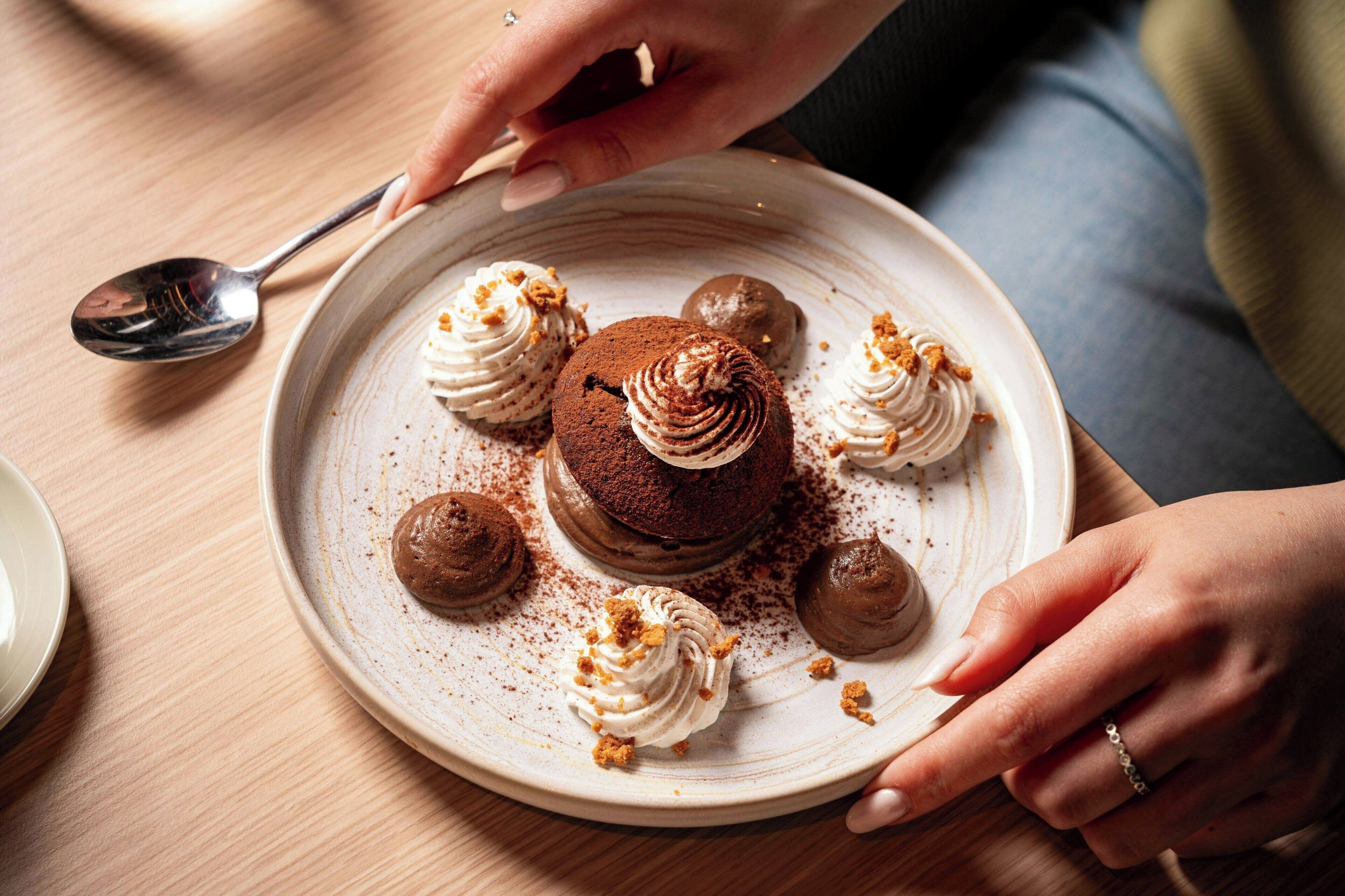 Een nagerechtopstel met chocoladetaart, slagroom en chocoladebolletjes op een keramieken bord.