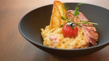 A bowl of food with pasta, a slice of meat, a cherry tomato, and a piece of bread.