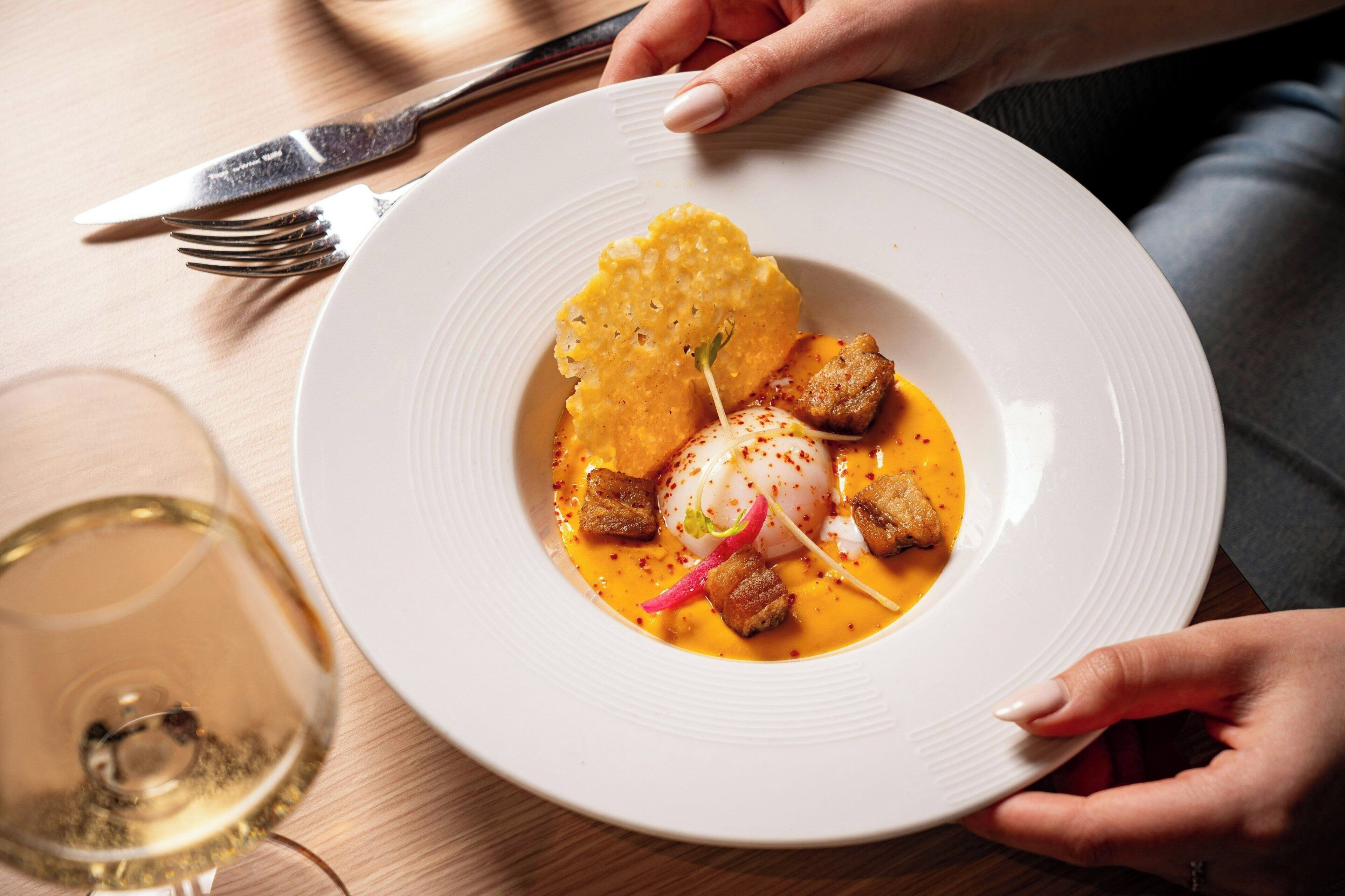 A plate of food with a white plate, a fork, and a glass of white wine on a wooden table.