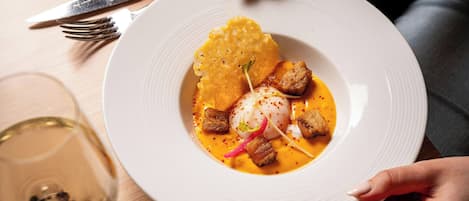 A plate of food with a white plate, a fork, and a glass of white wine on a wooden table.